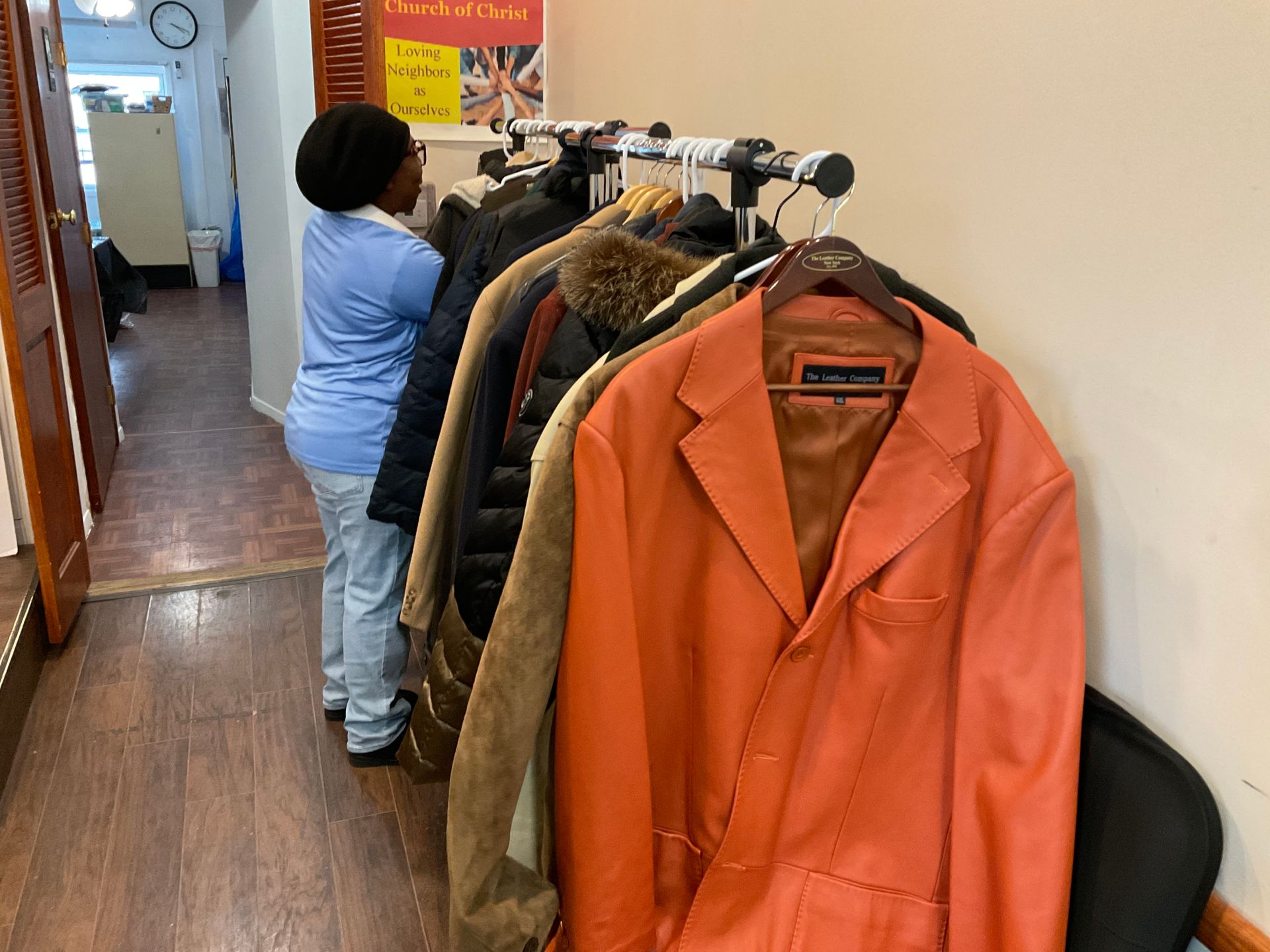 Person selecting a jacket from a rack in a narrow hallway. Coats in various colors hang on the rack.