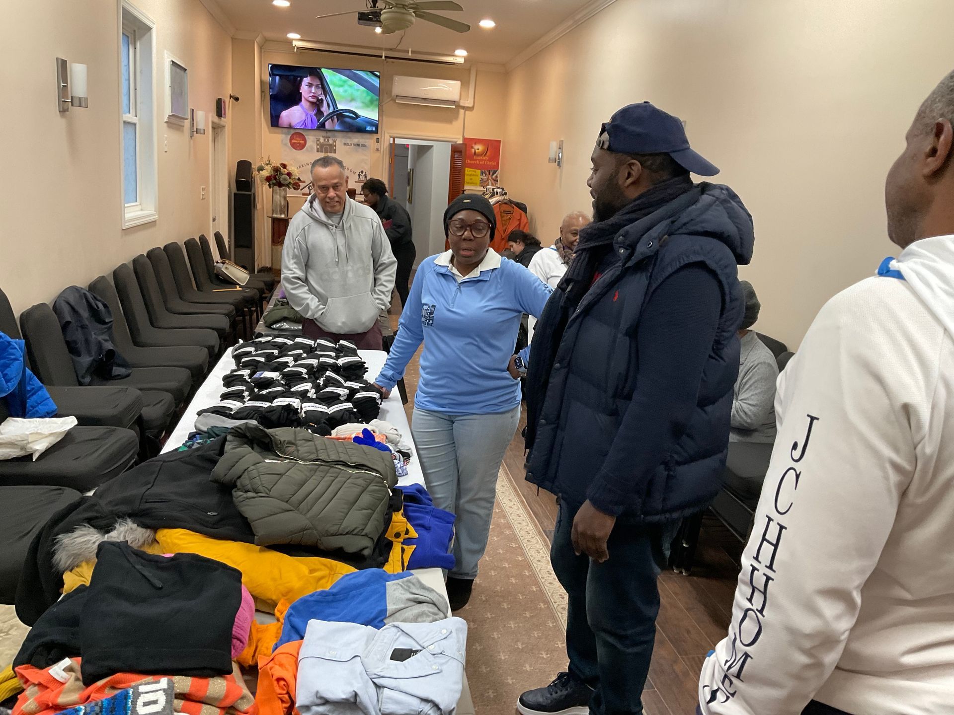 People examining clothes spread on tables inside a room, possibly a donation center.