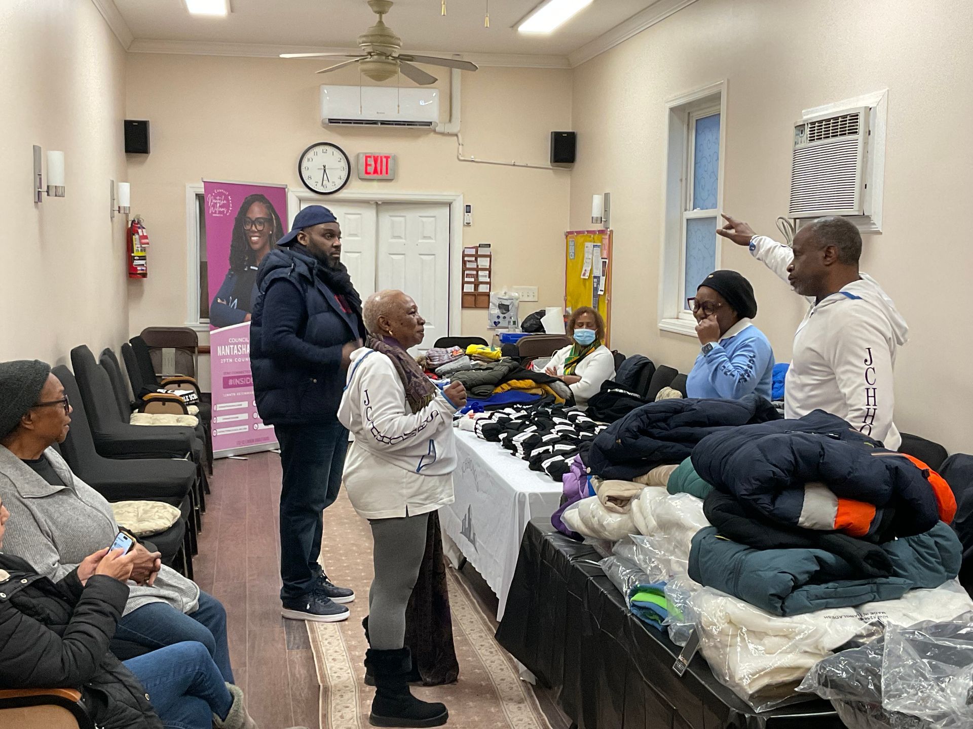 People at an indoor event, selecting items from tables of clothing and blankets.