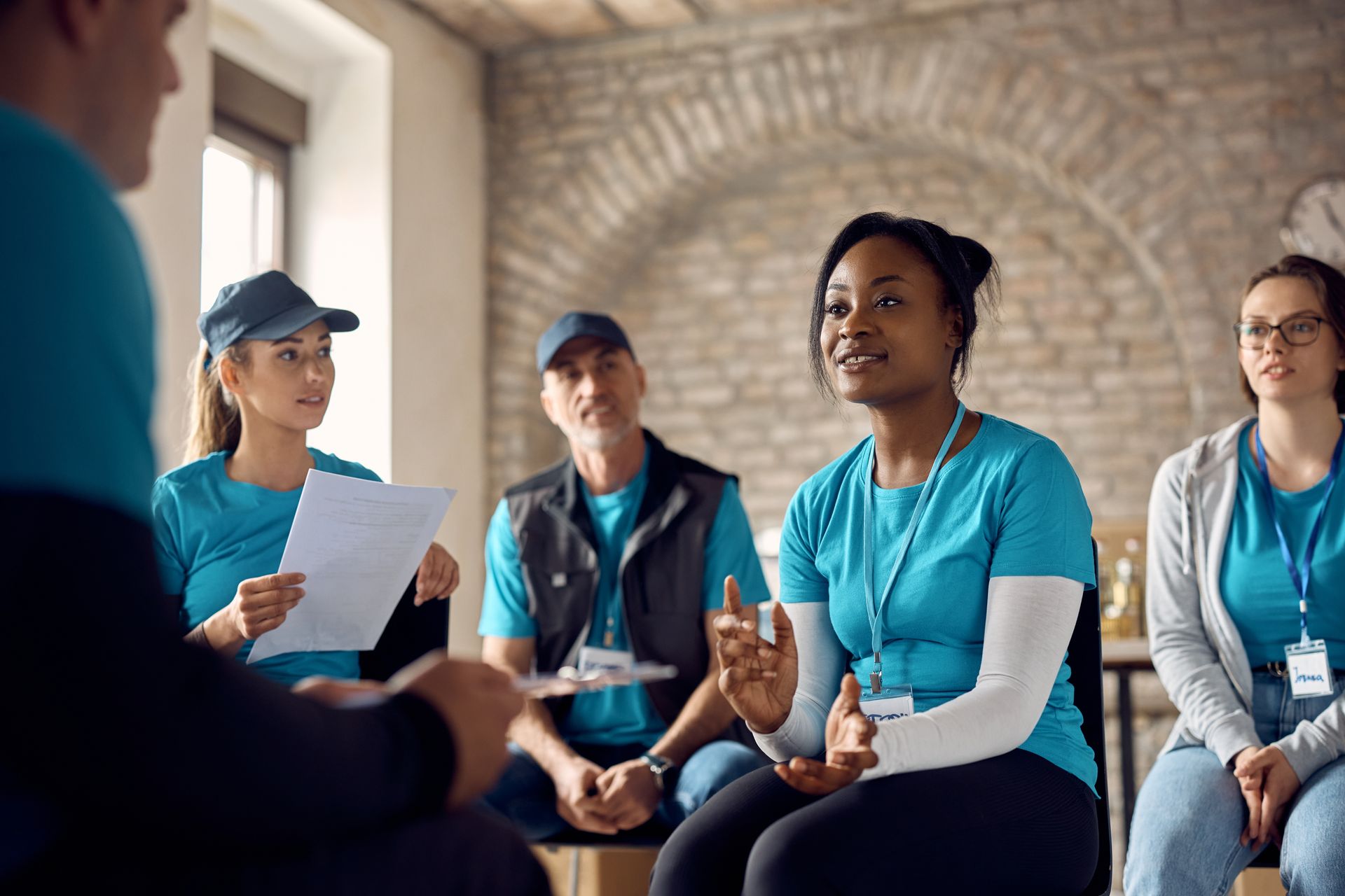 Group of people in blue shirts in a discussion circle, one woman gesturing while speaking.