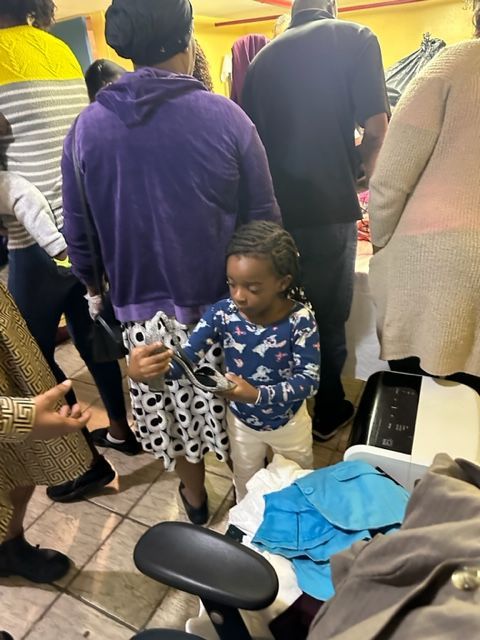 A group of people are standing around a little girl holding a cell phone