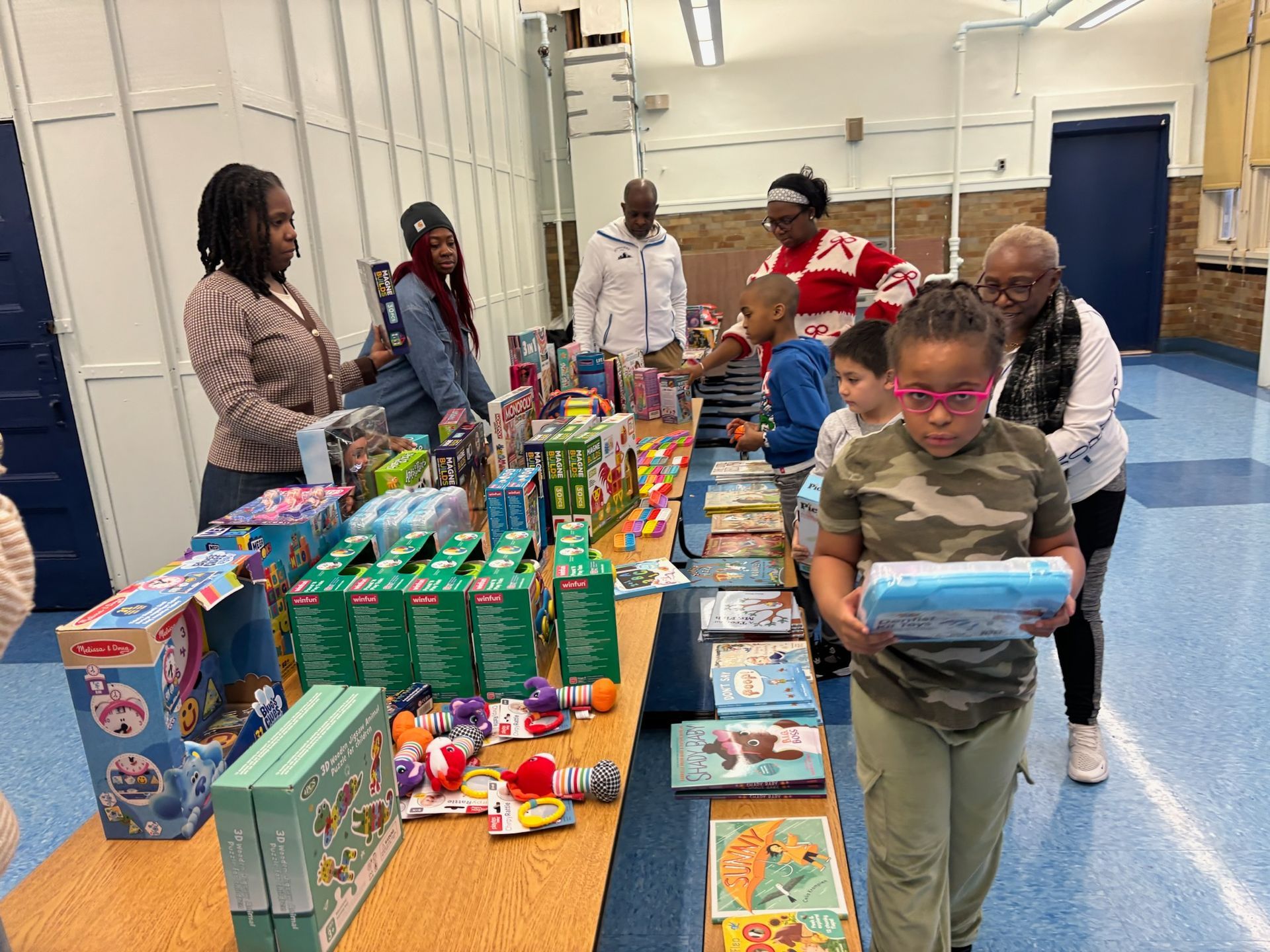 People at a table selecting gifts, with a variety of toys and books. Indoors, well-lit.