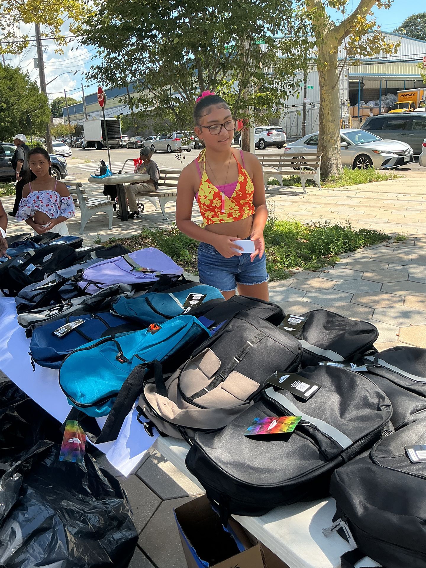 Woman browsing backpacks and bags at an outdoor market stall under trees.