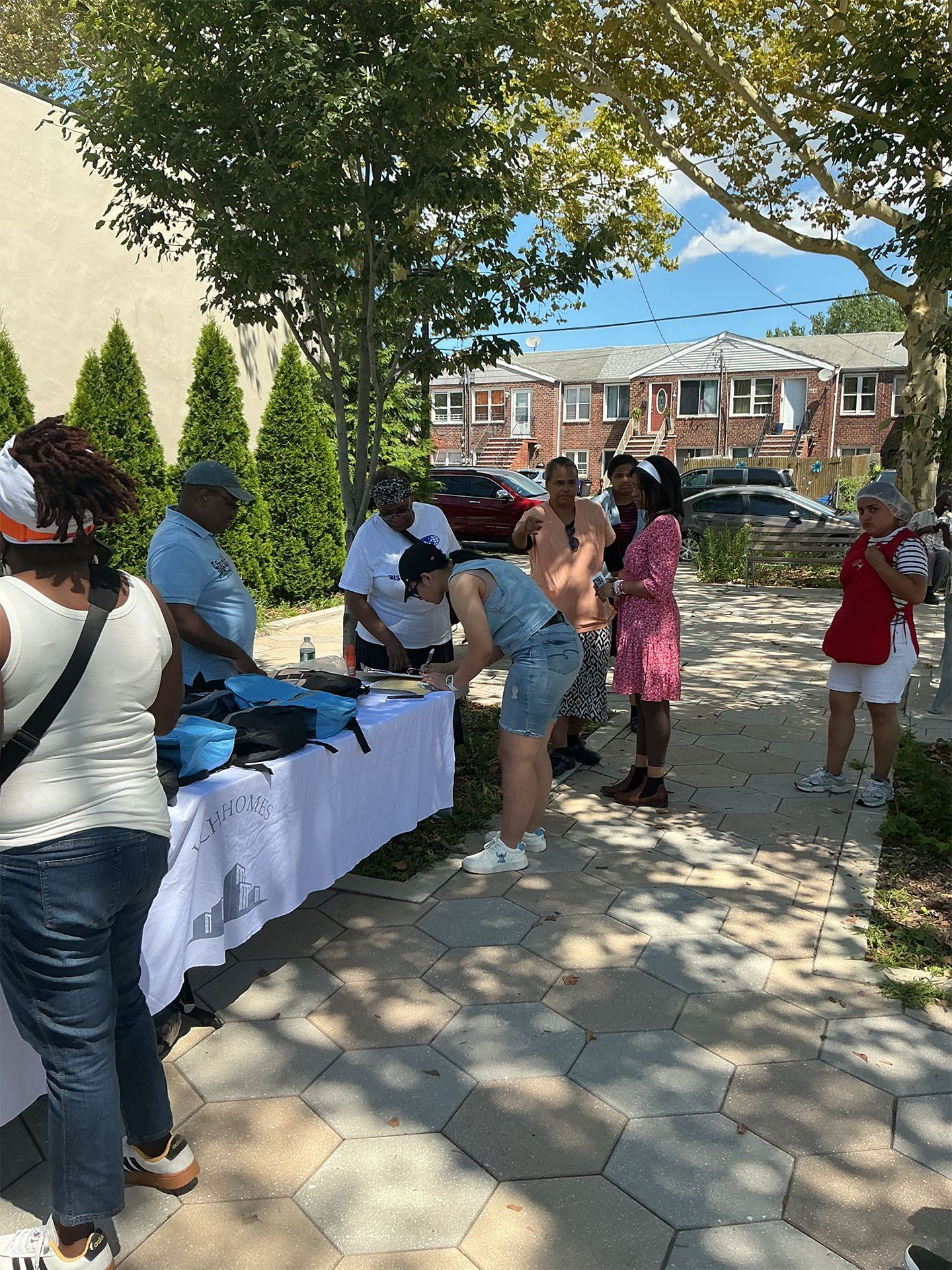 People browsing a table at an outdoor event under trees on a sunny day.