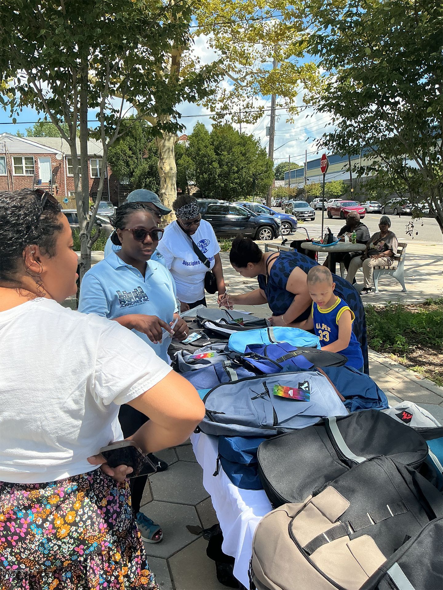 People gathered at a sidewalk table outdoors, sorting clothes and items on a sunny street.