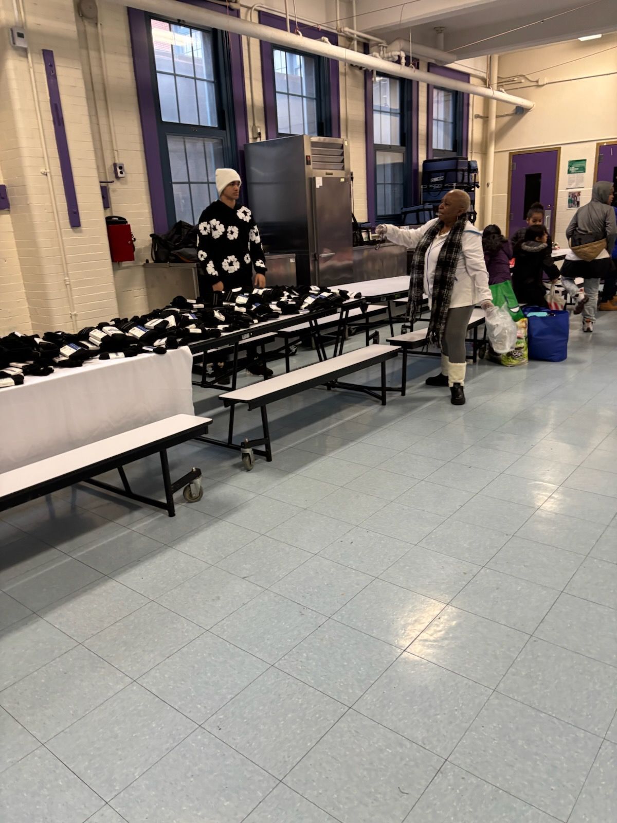 People in a school hallway with benches and items on them. One person points, another stands nearby.