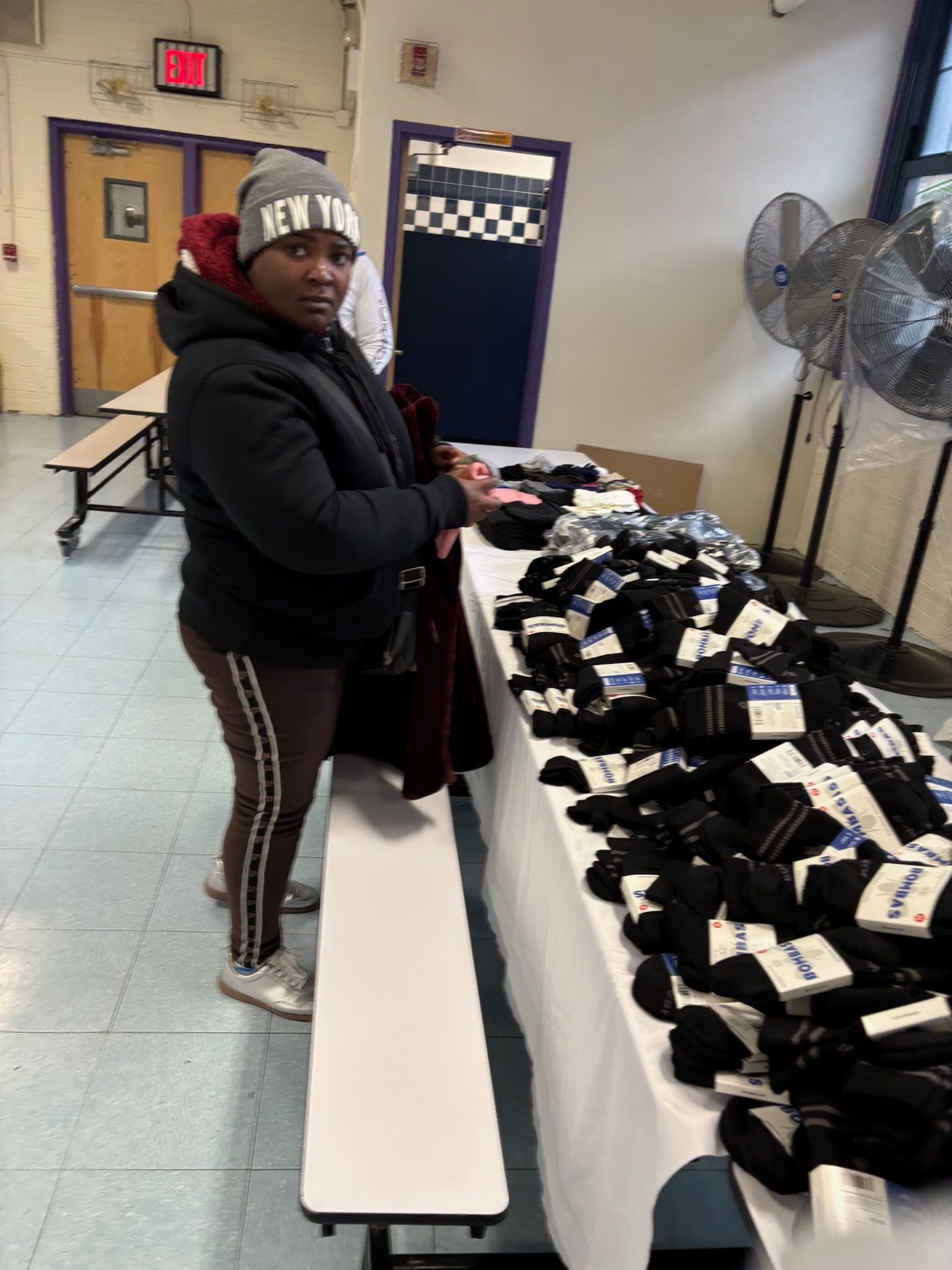 Person at table with many pairs of socks. She is wearing a jacket and hat inside a building.