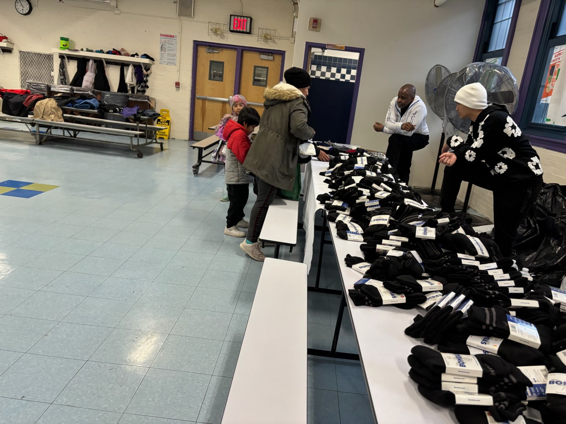 People selecting socks from tables in a school gymnasium.