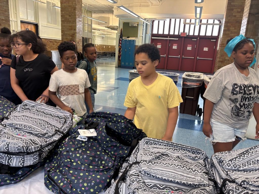Children looking at backpacks in a hallway; some are wearing t-shirts.