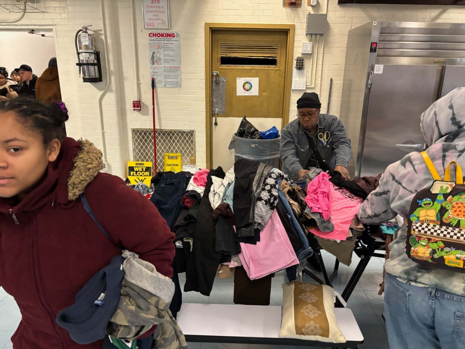 People sorting clothes at a donation site. Clothes are piled on tables. One person looks at the camera.