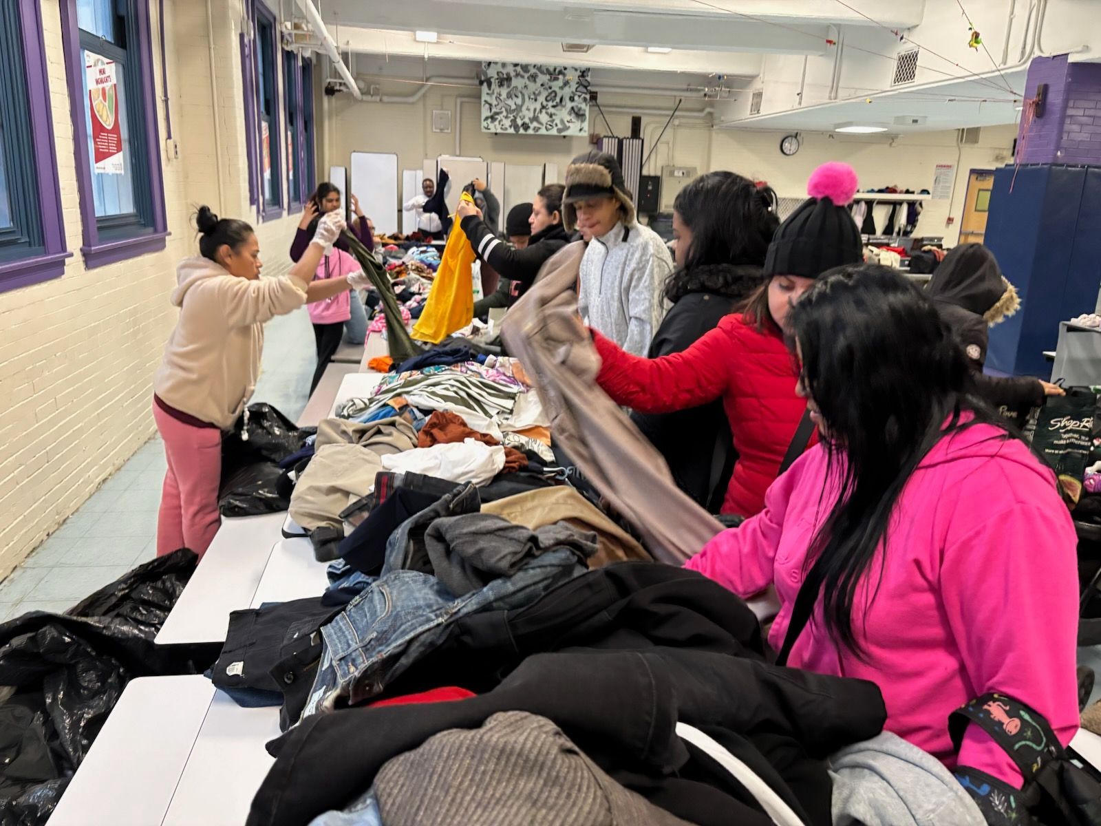 People browsing clothing displayed on tables in a brightly lit room.