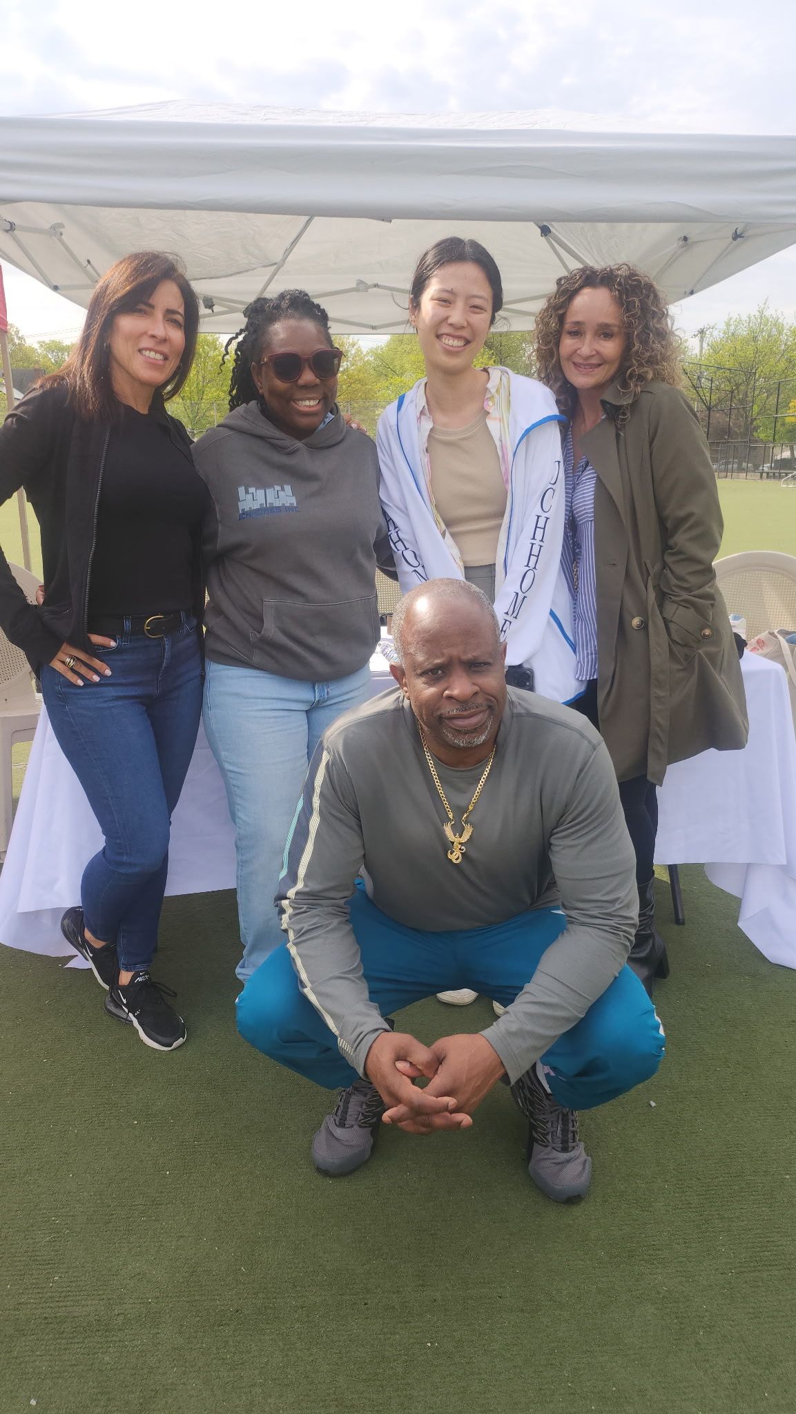 Group of six people posing outdoors. One man squats, the others stand smiling.