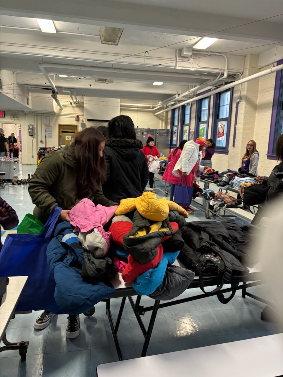 People sorting through clothes on tables indoors, possibly a donation event.