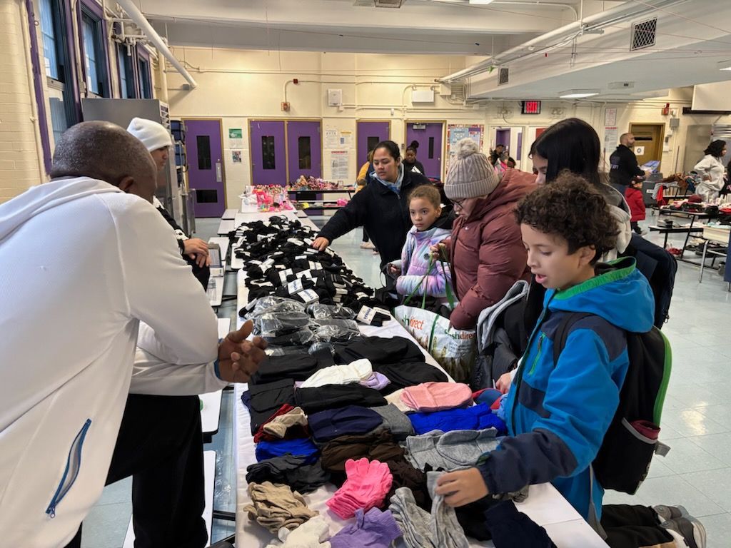 People browsing and selecting gloves and scarves at a table in a school cafeteria.