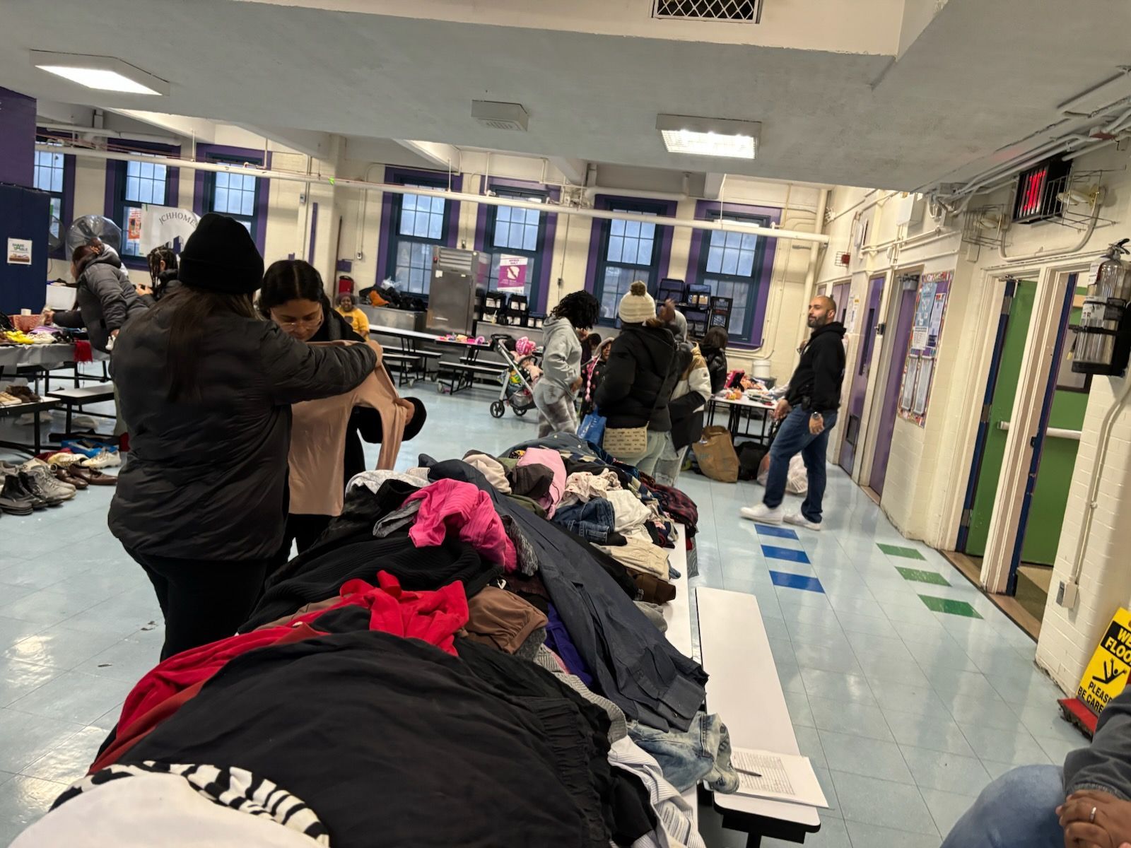 People sorting clothes on tables in a room with blue floors and white walls; possible donation event.