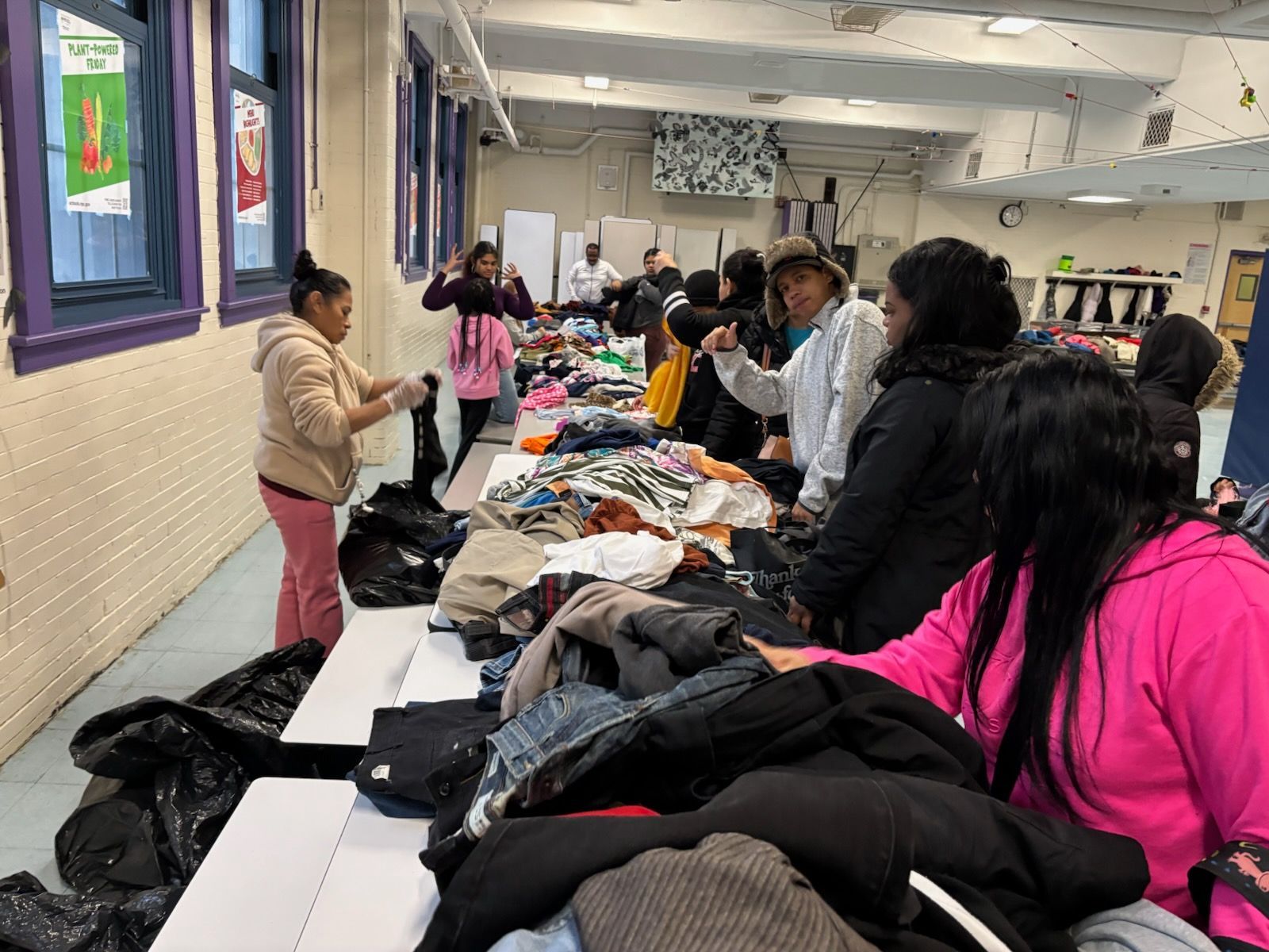 People browsing and selecting clothes from tables in a community center.