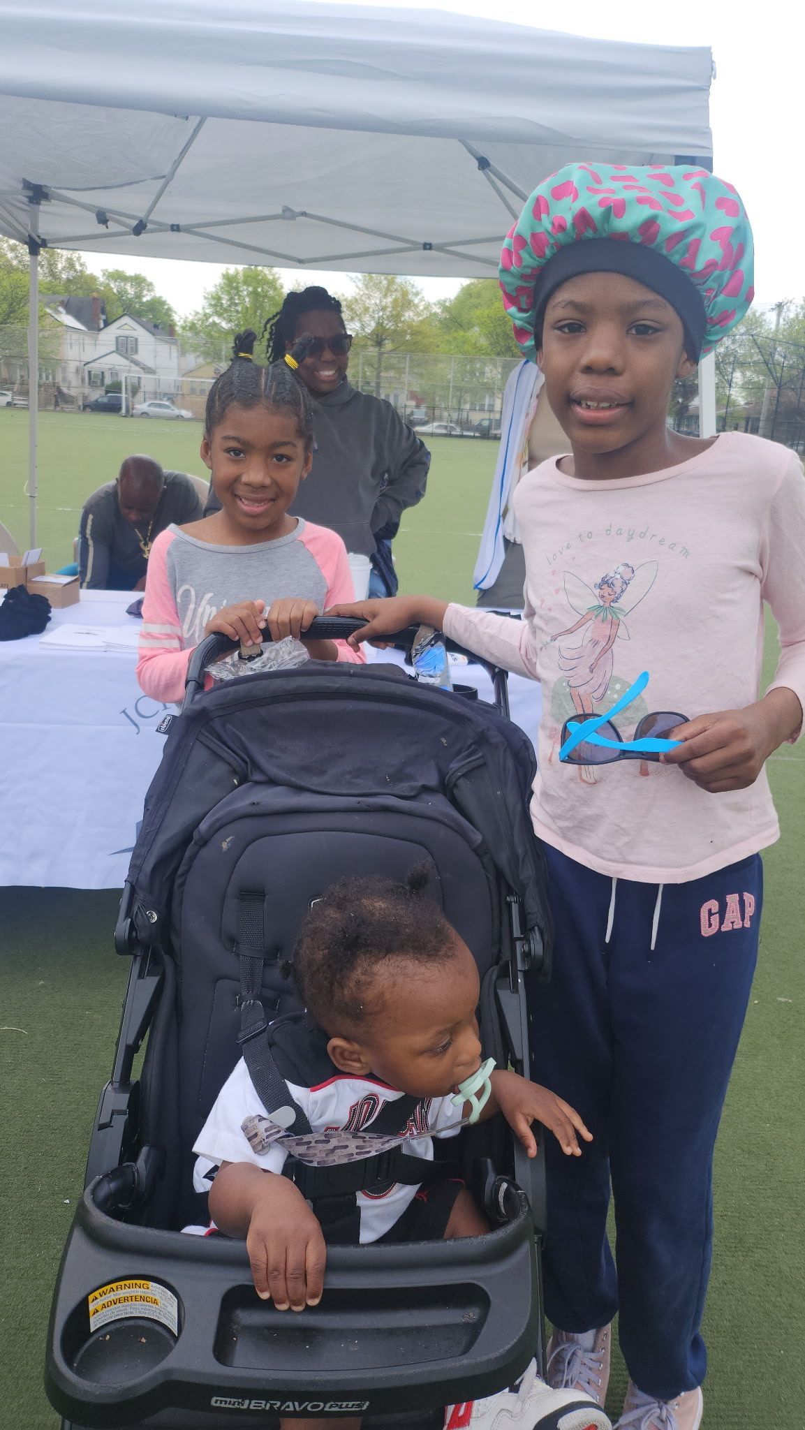 Three children and a baby in a stroller posing outdoors under a tent.