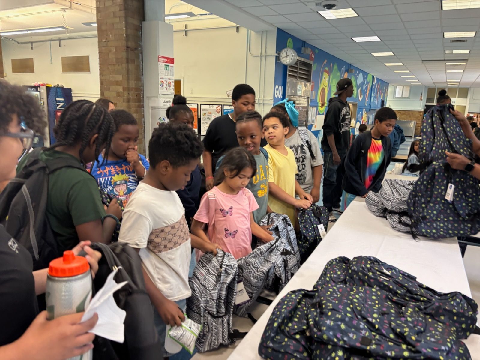 Children gather near a table with backpacks, possibly at a school or community event.