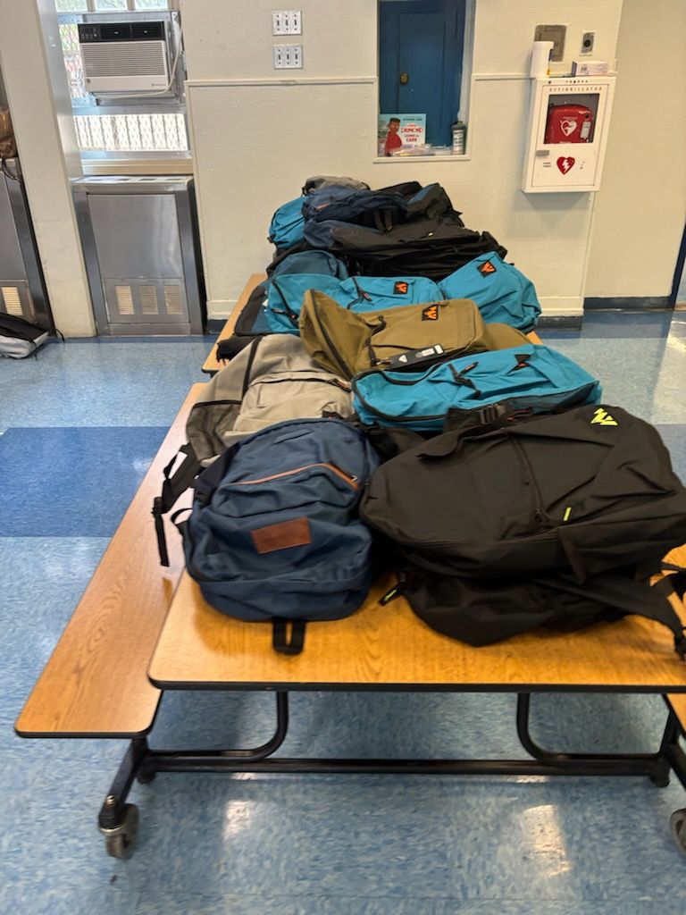 Backpacks piled on a school cafeteria table; various colors.