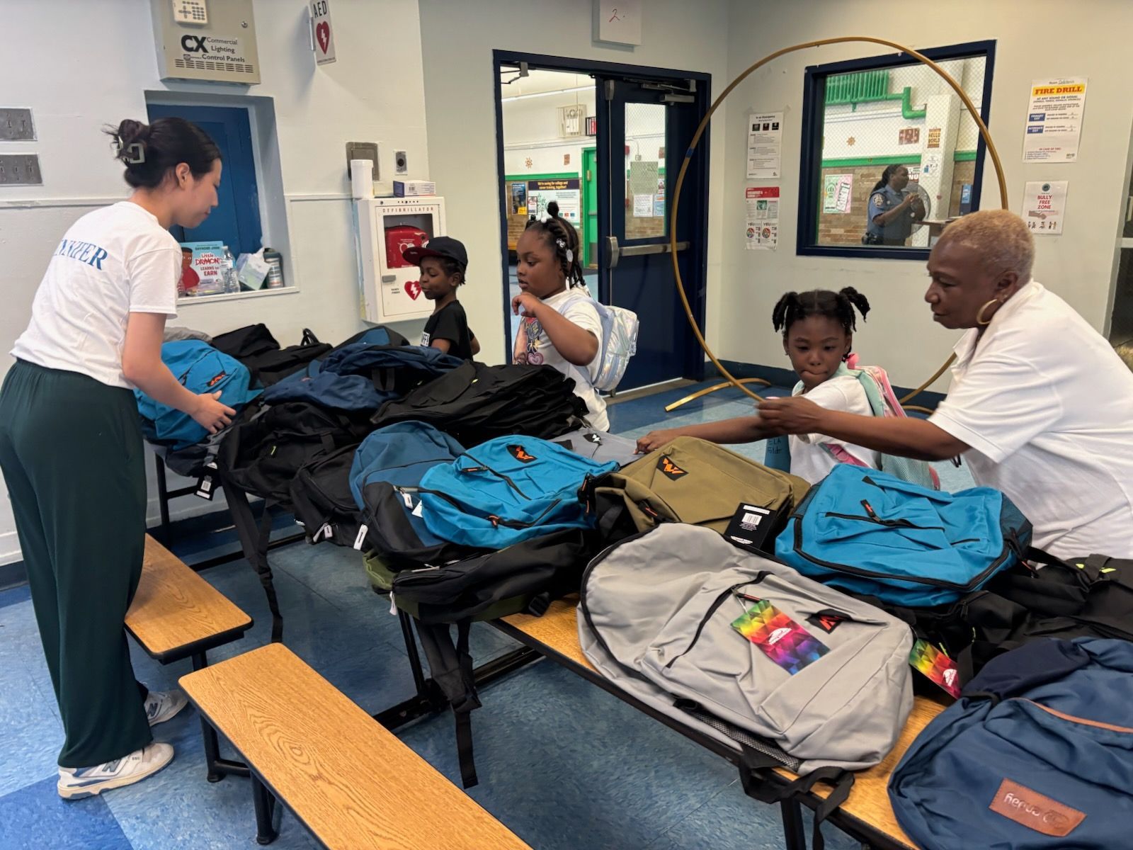 People distributing backpacks to children in an indoor setting.