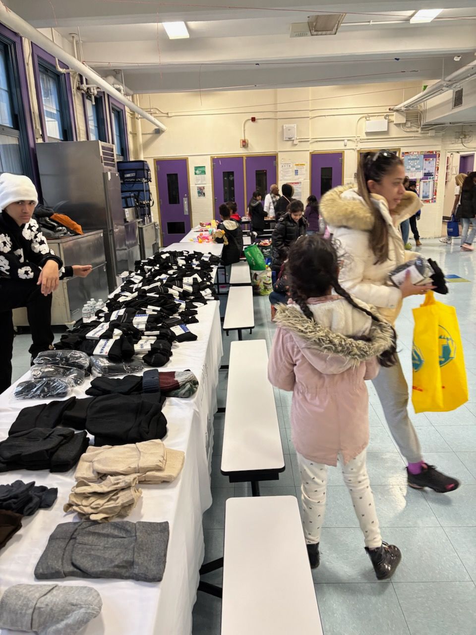 People selecting winter clothing laid out on tables in a school cafeteria.