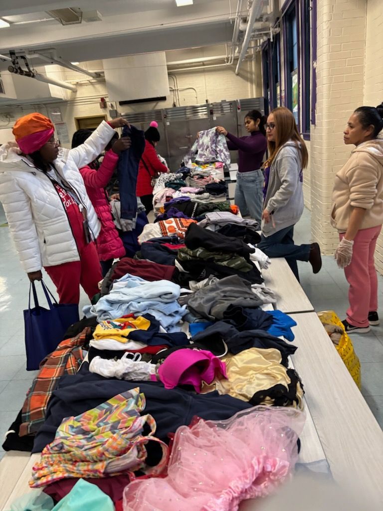 People selecting clothes from a table covered in garments. Interior, fluorescent lights.