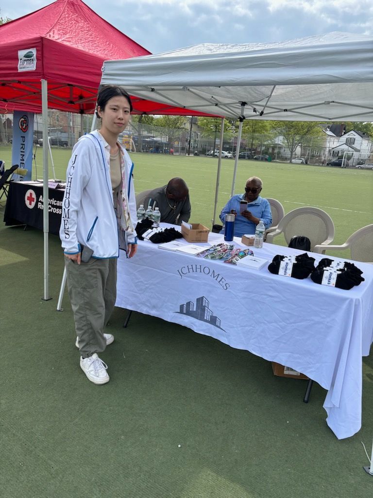 Person standing at a table under a tent. Table displays socks and merchandise. Other people in the background.