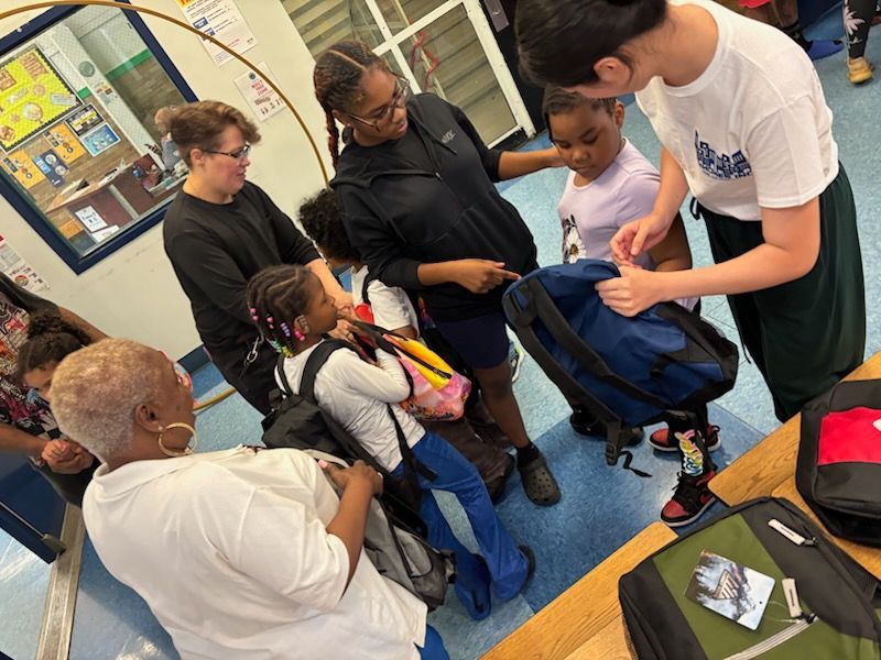 People assisting children with backpacks in a school hallway.