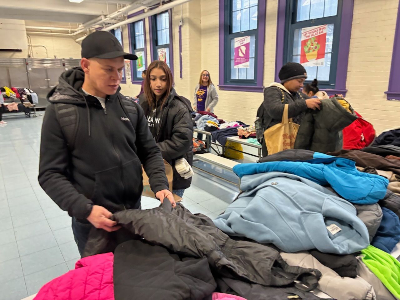 People sorting through clothing donations in a room. Piles of jackets on a table, others looking through them.