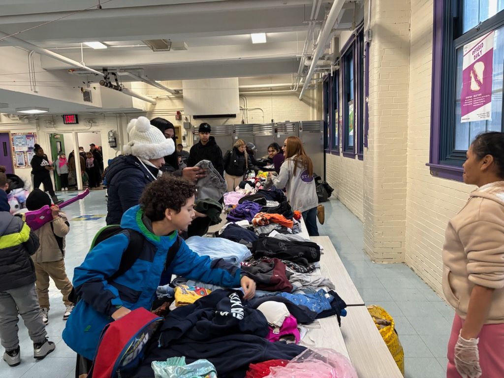 People browsing clothing laid out on tables in a school hallway.