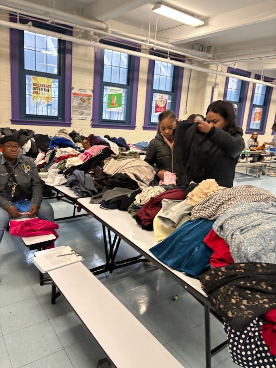 People sorting clothes on tables in a room with windows.