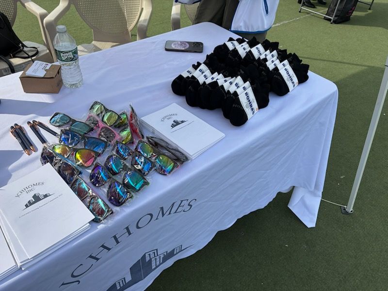 Table with sunglasses, socks, notebooks, pens, and water bottle on green surface. 