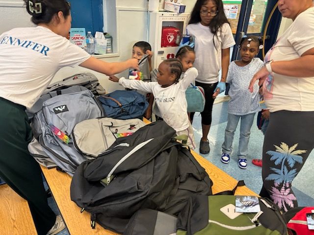 People selecting backpacks from a table; a person with 