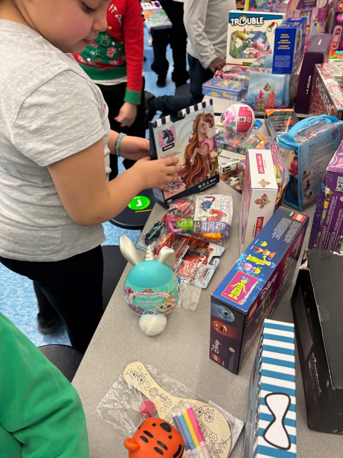 Person looking at toys on a table with other people and toys in background.