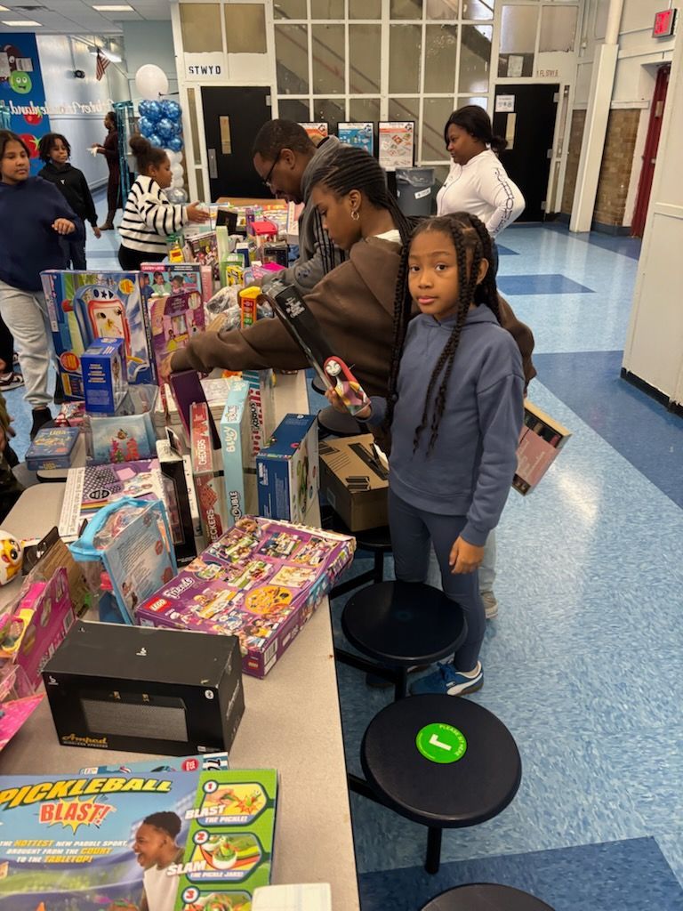 People browsing toys displayed on tables in a brightly lit room. A young girl looks at the camera.