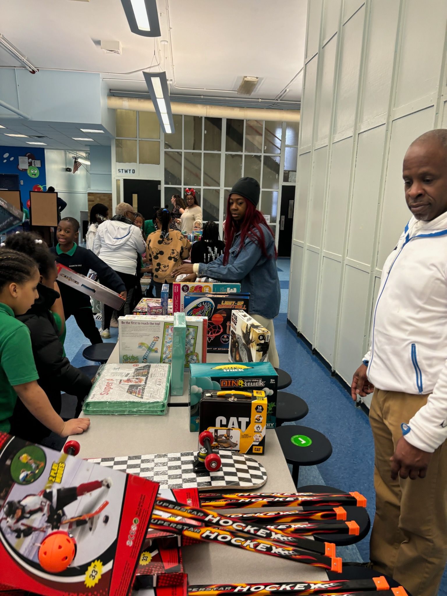 Children and adults at a table with toys and gifts, possibly at a school or community event.