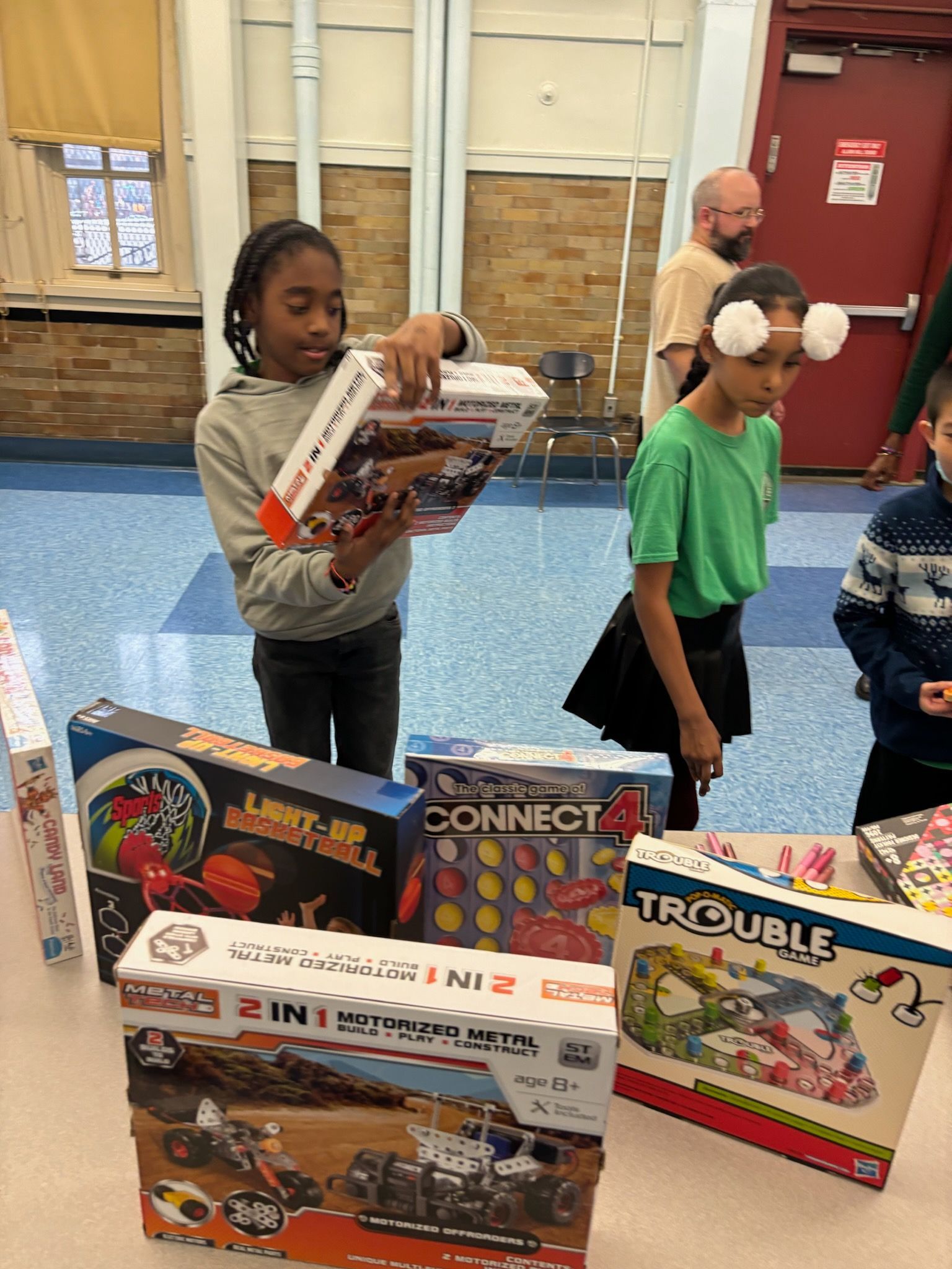 Children examining board games in a school setting. One child holds a box. Others look on.
