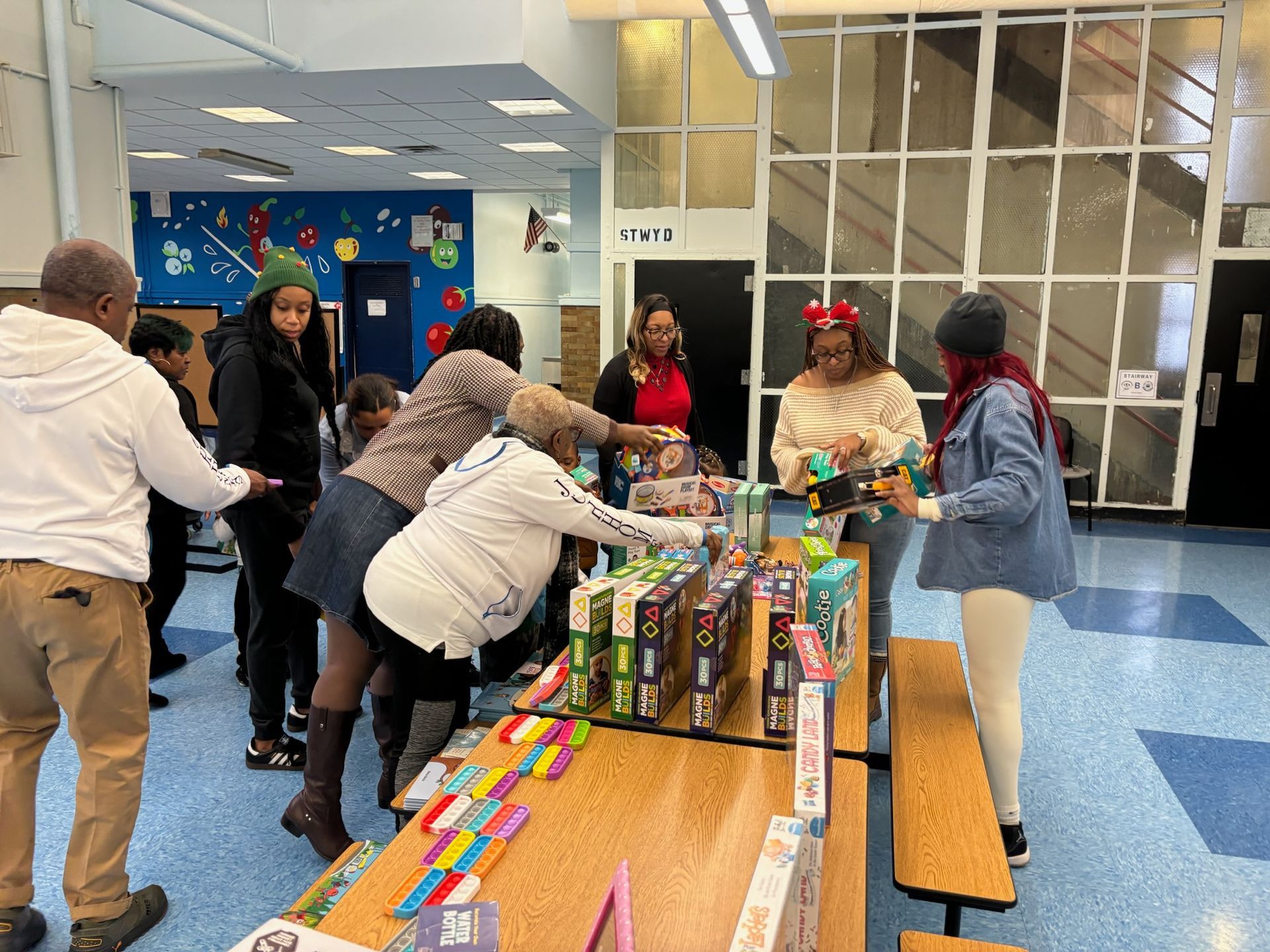 People gather around a table displaying toys. A school hallway is the setting.
