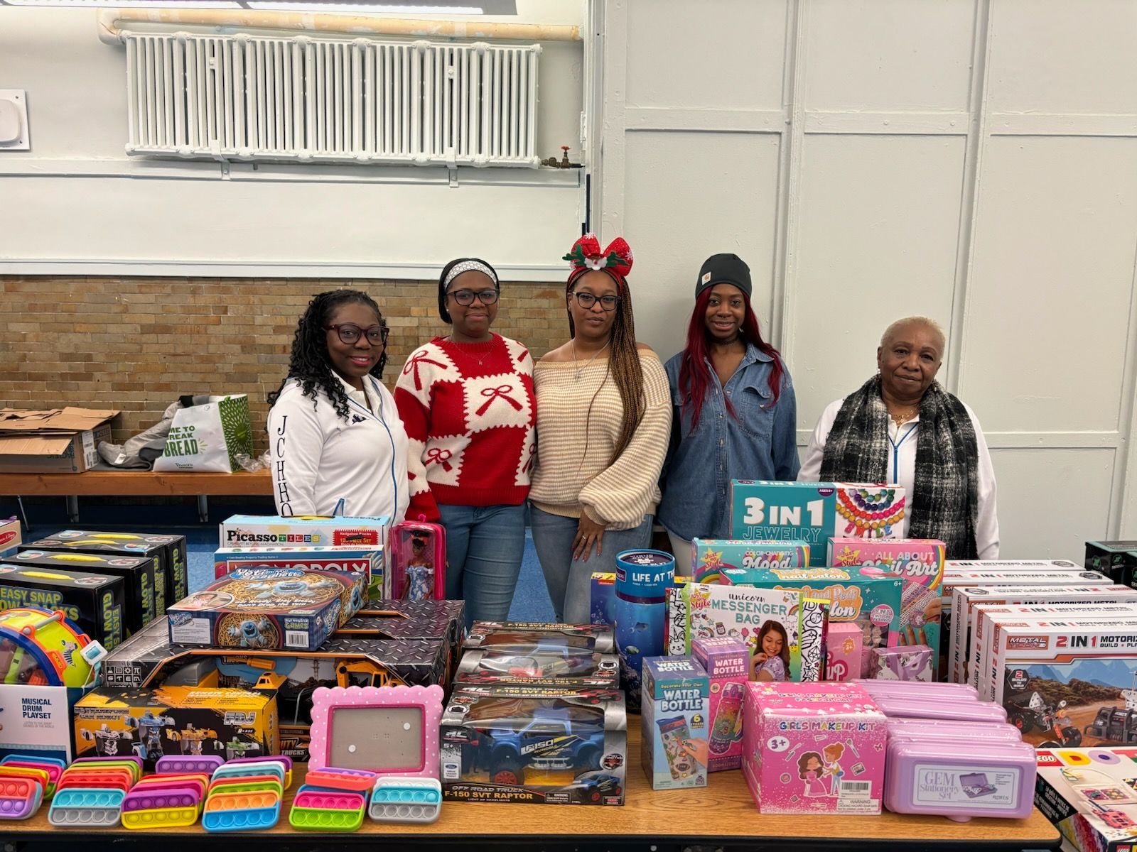 Five people pose behind a table laden with toys and gifts in a brightly lit room.