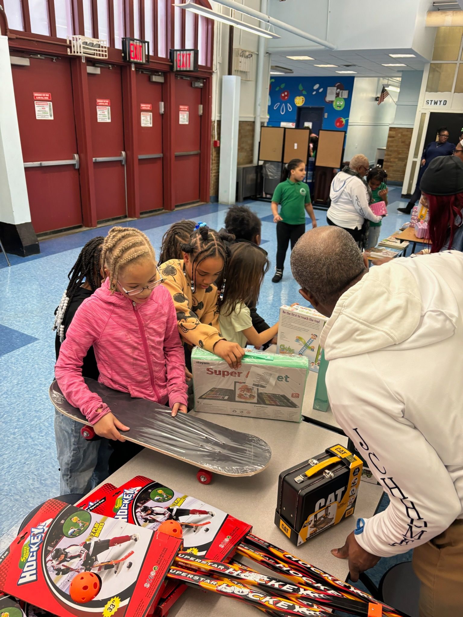 Children and adults look at toys on a table in a school.