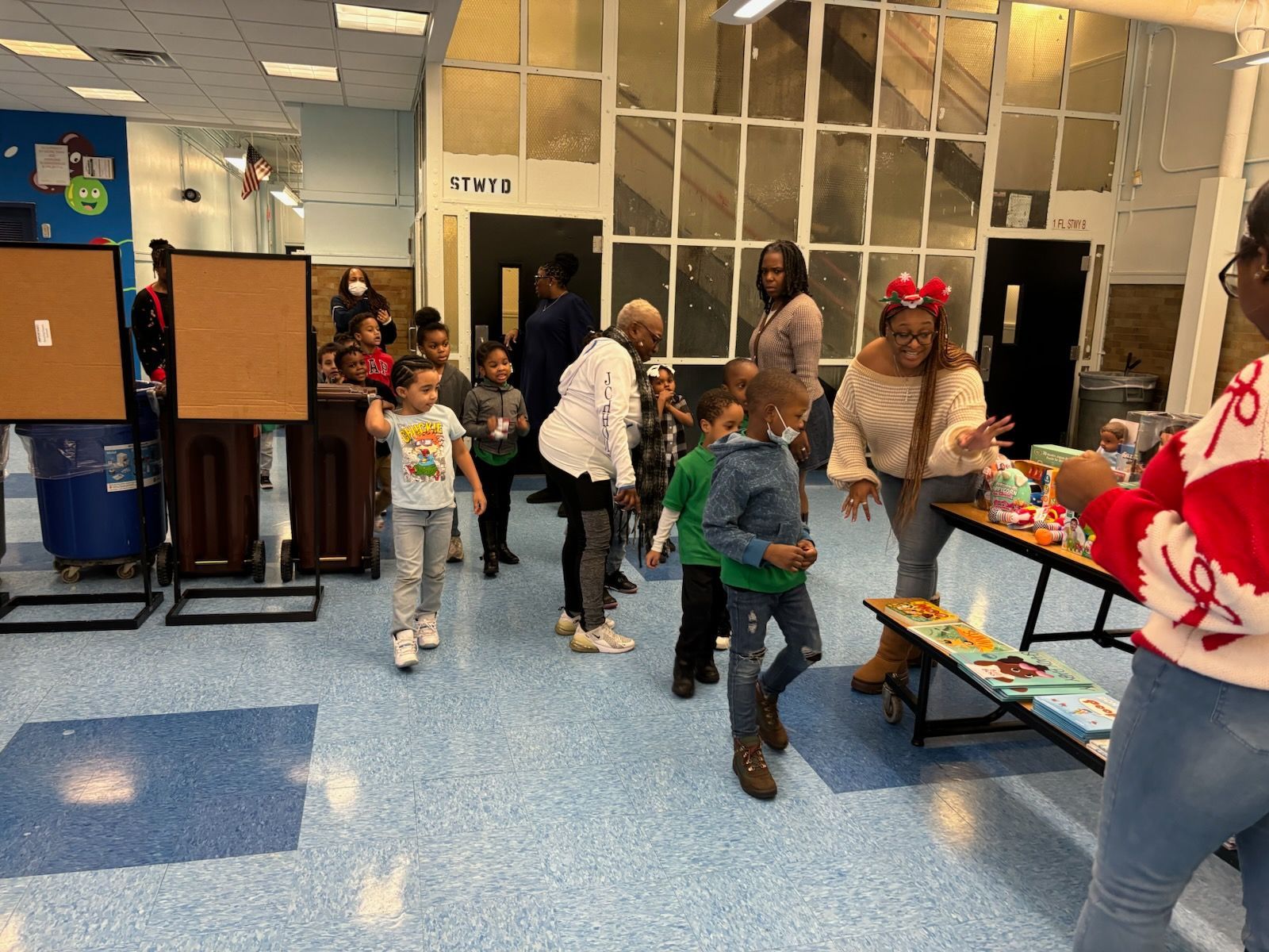 Children and adults in an indoor space near a table with items, some dancing and interacting. Blue floor.