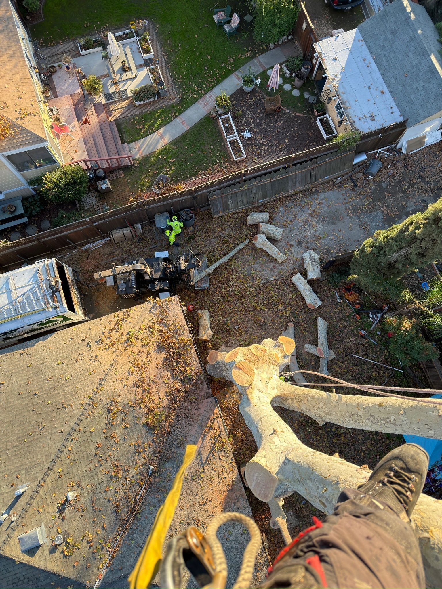 View from a height shows debris on a flat roof. A person in work clothes and a harness is visible.