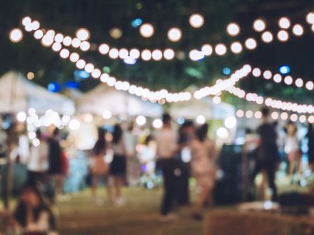 Crowd at an outdoor evening event under glowing string lights, softly blurred.