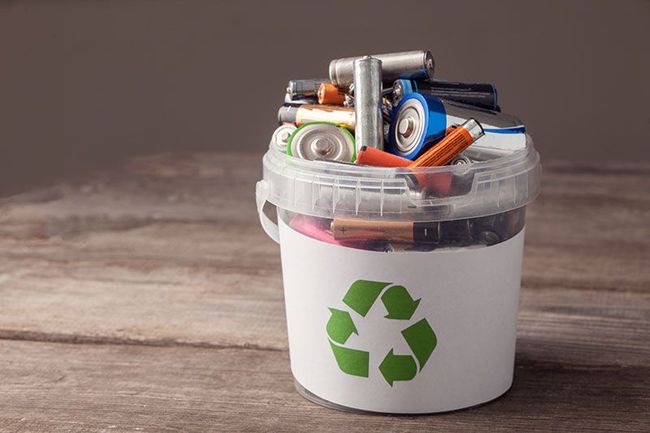 Recycling bin filled with assorted electronics and batteries on a wooden surface
