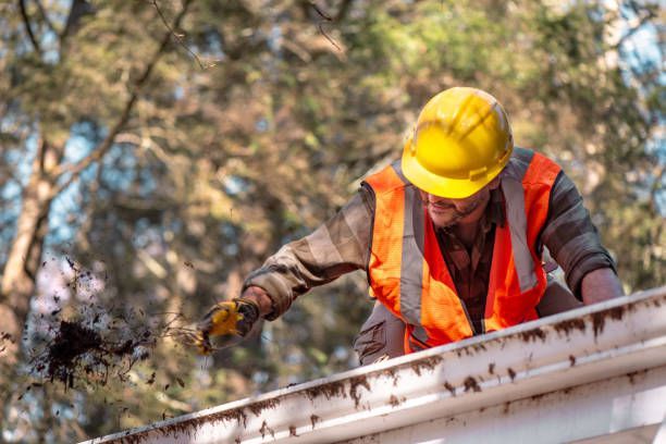 Service technician pressure washing debris from gutters.