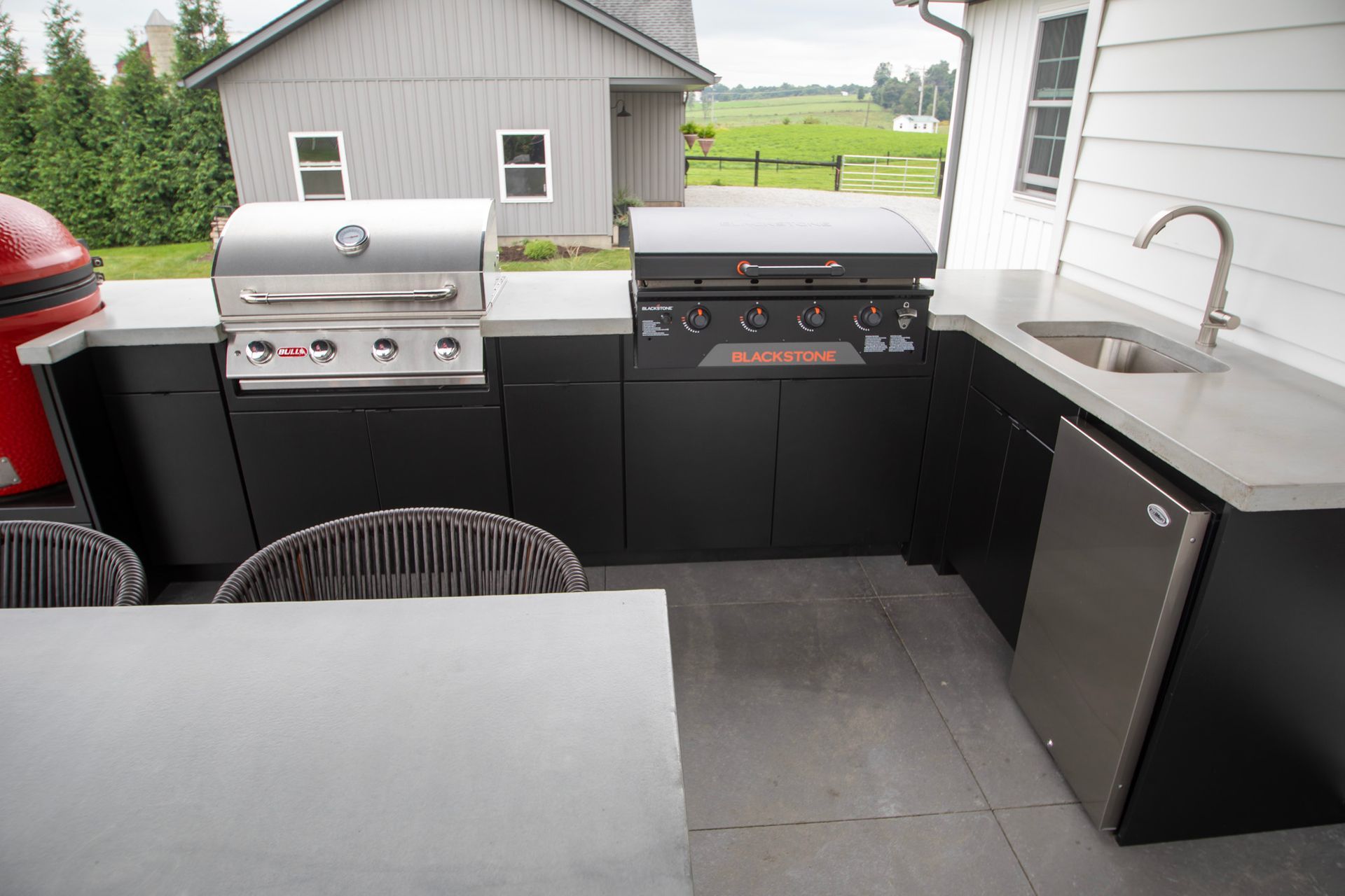 Outdoor patio with grill, sink, and mini fridge beside a table and chairs