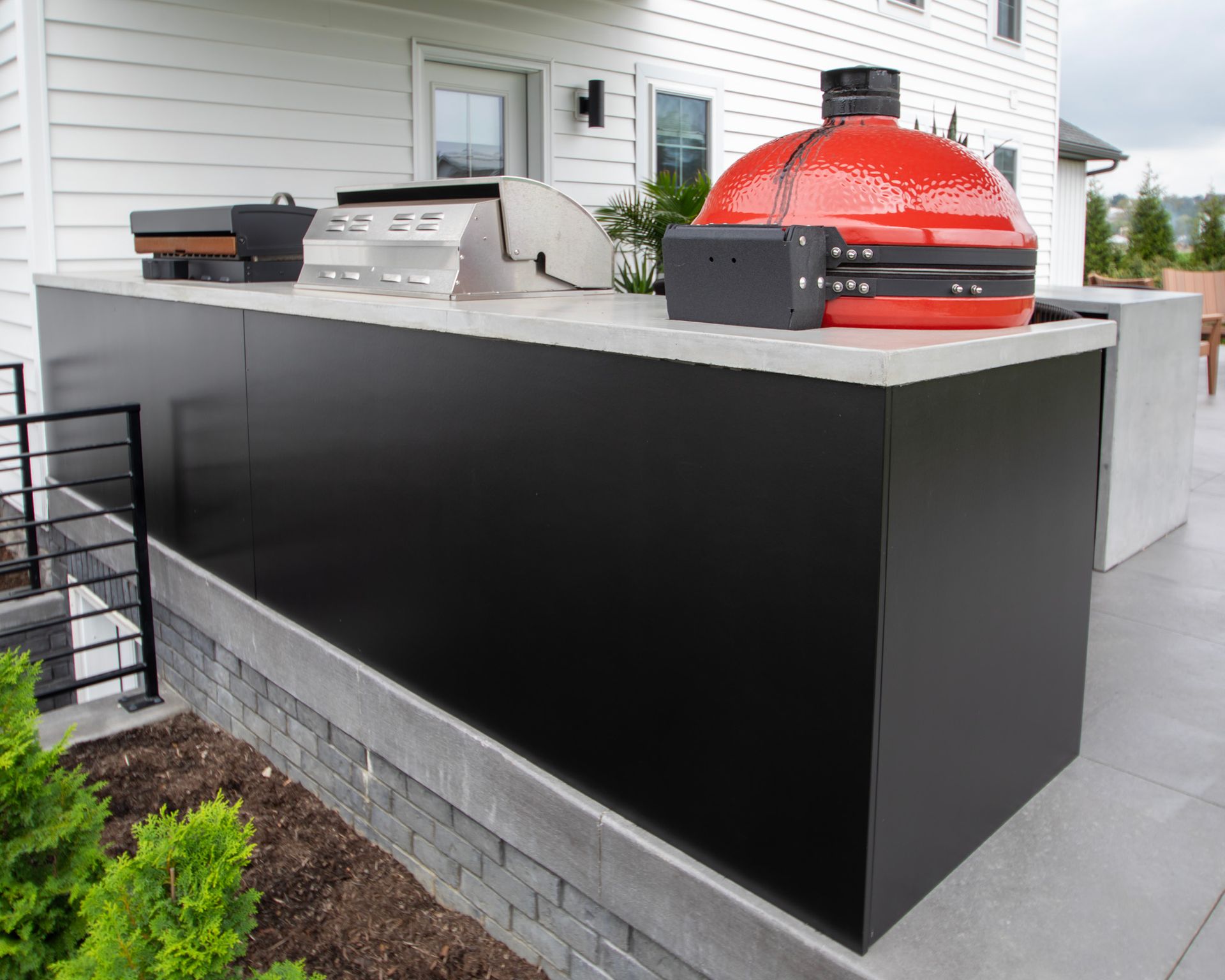 Modern outdoor patio with a red dome pizza oven and black counter on a concrete deck