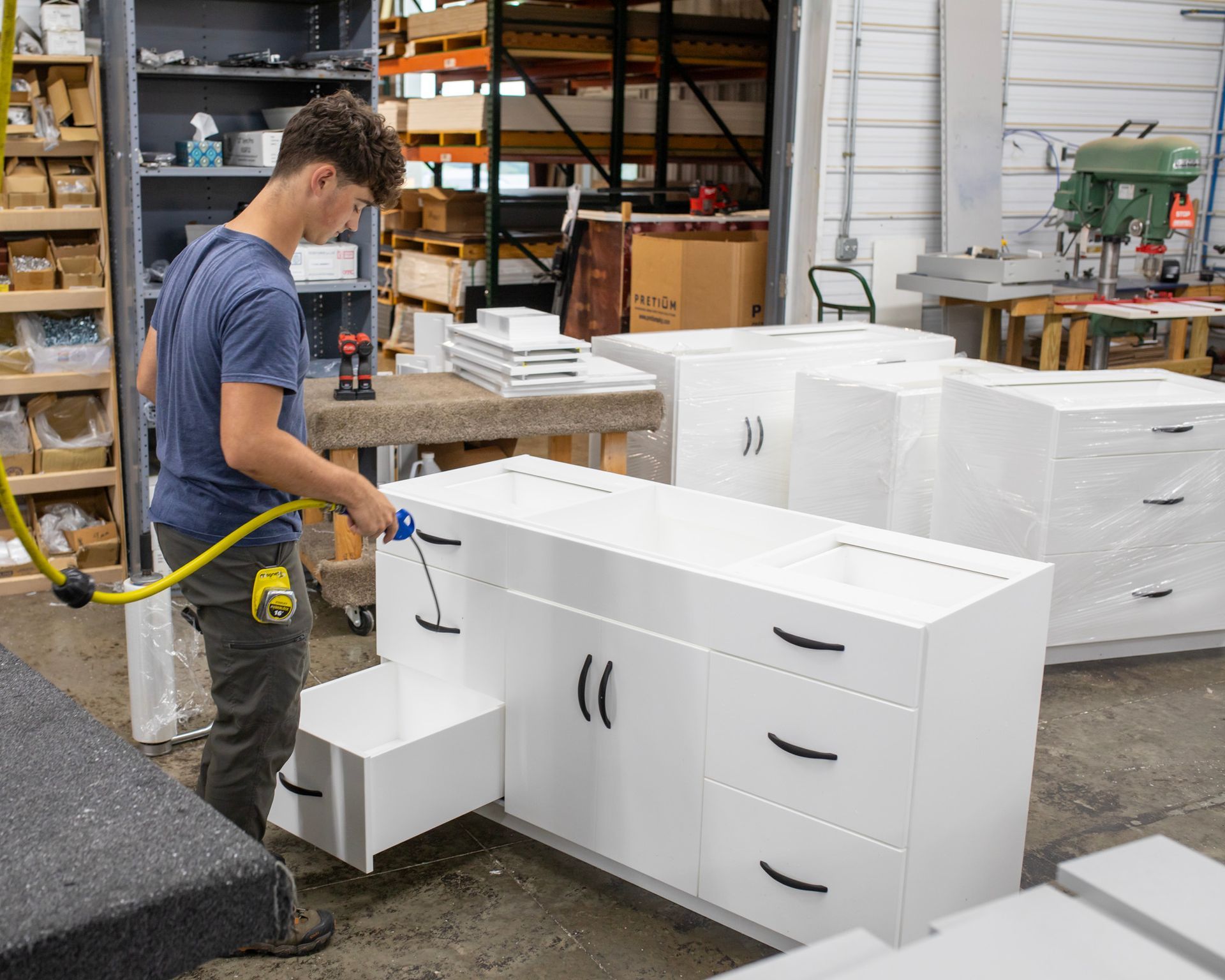 Worker assembling white cabinets in a workshop with shelves, tools, and storage boxes in the background