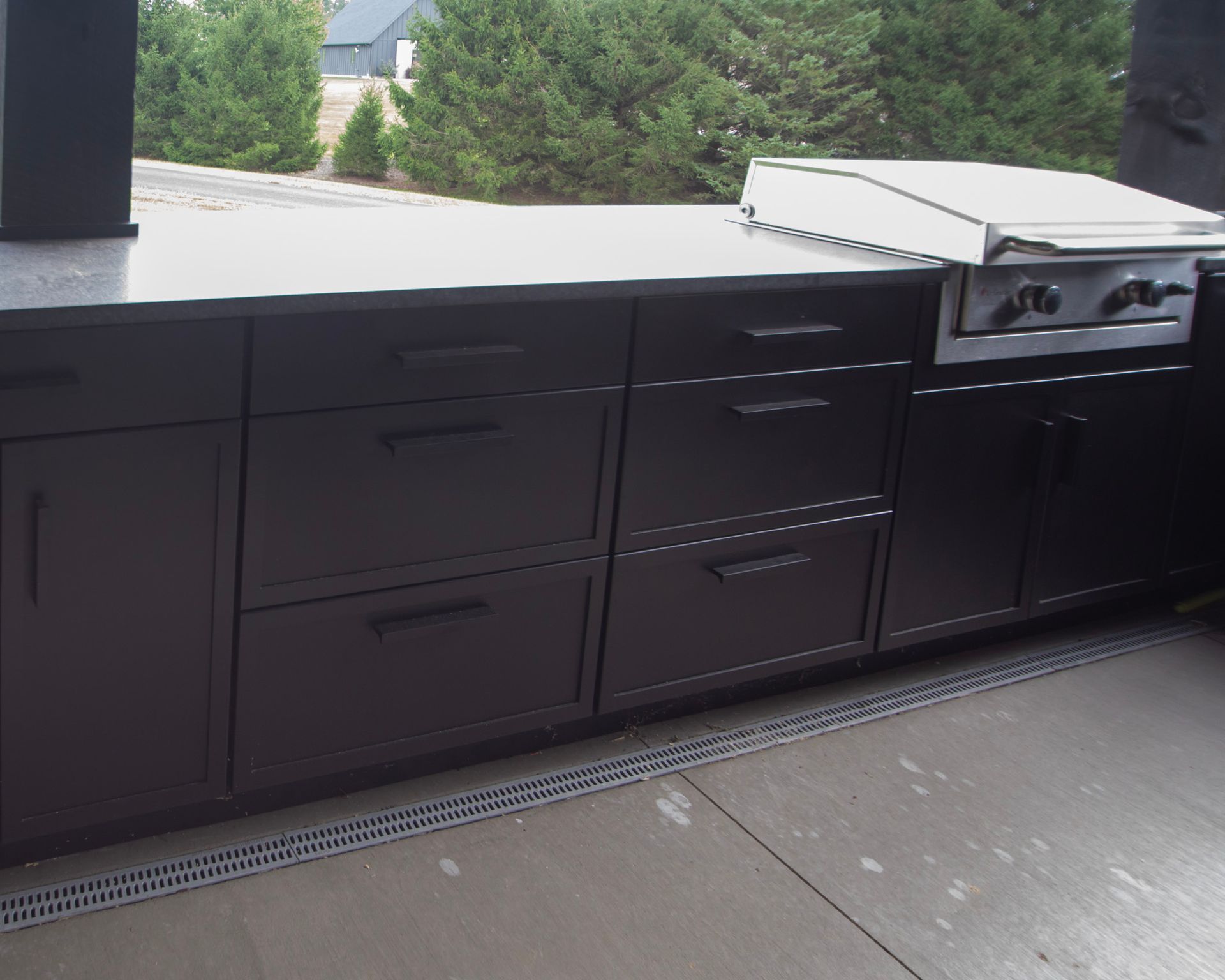 Black outdoor kitchen cabinets with built-in grill on a patio, overlooking trees and a distant mountain.