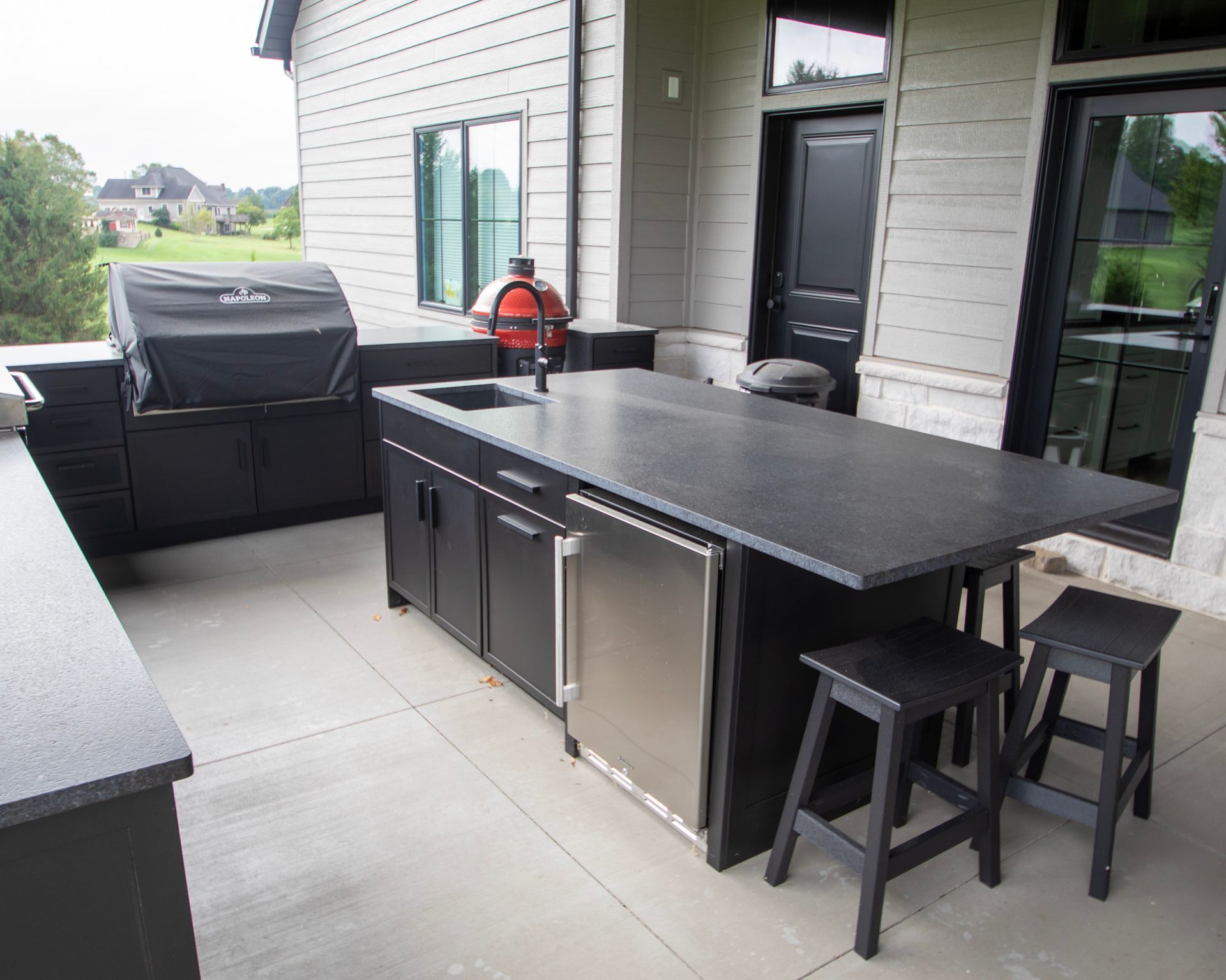 Outdoor patio with black grill, bar counter, stools, and a small fire extinguisher beside a house